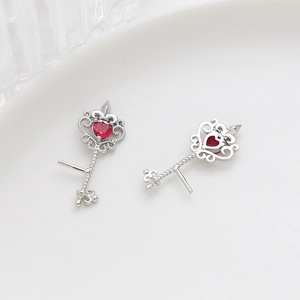 Macro shot of silver key-shaped earrings featuring red heart-shaped gemstone accents