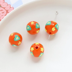Close-up of orange acrylic round beads with heart and star patterns for DIY jewelry creation.