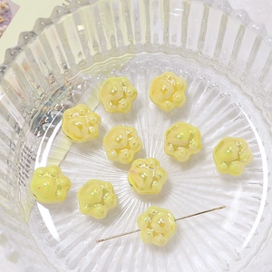 Macro detail of yellow ceramic cat paw beads with metal needle showing the drill hole