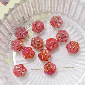 Macro detail of glossy dark red ceramic cat paw beads for DIY jewelry making in a glass bowl