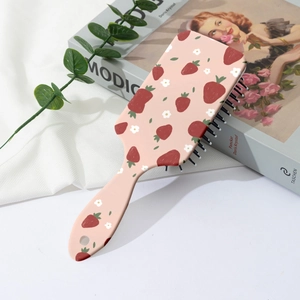 Détail d'une brosse à cheveux rose avec motifs de fraises et fleurs sur un bureau