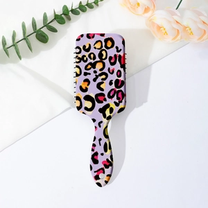 Close-up of leopard print hairbrush with air cushion on clean white fabric backdrop