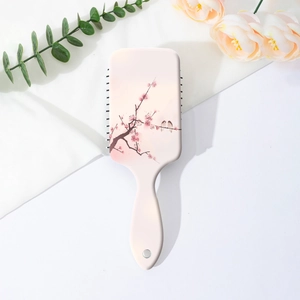 Detail of pink paddle brush featuring floral cherry blossom and bird prints on the back