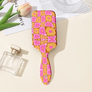 Detailed close-up of a pink and yellow floral checkered air cushion hairbrush with hang hole
