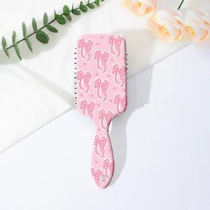 Vue à plat d'une brosse à cheveux rose à nœud sur textile blanc avec fleurs douces