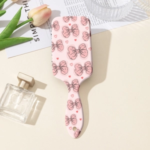 Détail d'une brosse à cheveux à coussin rose avec imprimés nœuds sur un bureau esthétique