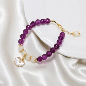 Detail of beaded bracelet with purple beads, gold hardware, and a cloud-shaped shell pendant