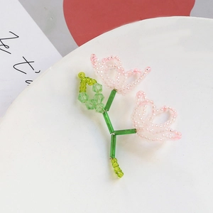 Macro shot of handmade beaded pink flower pendant with green stem on white plate