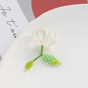 Detail of handmade beaded flower brooch with white petals and green crystal leaves