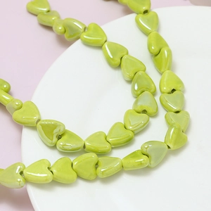 Macro shot of grass green ceramic heart beads on white plate for DIY jewelry