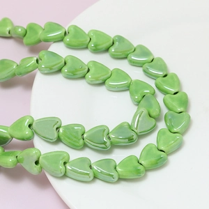 Macro shot of green heart-shaped ceramic beads for DIY jewelry with glossy finish