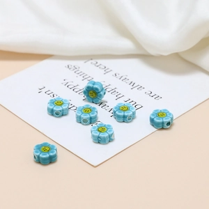 Macro detail of light blue ceramic flower beads with yellow smiley face for DIY jewelry