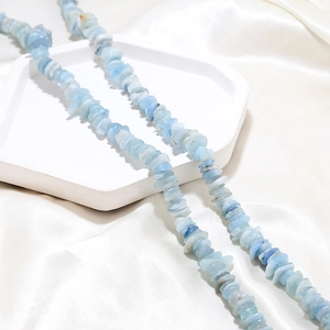 Macro shot of natural pale blue aquamarine crystal chips on white silk background