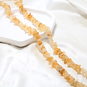 Macro view of irregular amber citrine crystal beads on white silk and marble display
