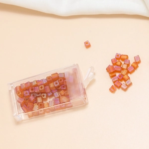 Macro view of 4mm orange-pink iridescent square hole glass beads in a clear box