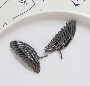 Détail macro de breloques plumes en métal noir pour bijoux DIY sur plateau blanc