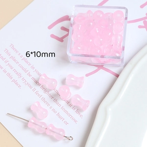 Détail de perles en verre haltère roses 6x10mm pour bijoux DIY dans une boîte transparente