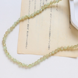 Détail de perles en cristal facetté vert menthe disposées en courbe S sur papier vintage