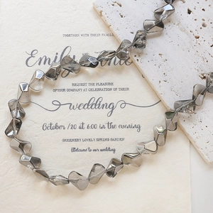 Macro shot of smoky grey faceted glass beads on textured stone and wedding invites