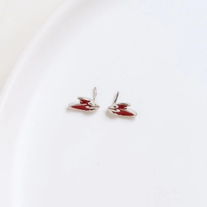 Macro view of red and silver wing-shaped enamel earrings on a white ceramic plate