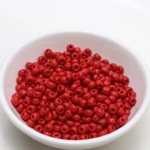 Detailed top view of 4mm red lacquered seed beads in a white bowl for DIY jewelry making