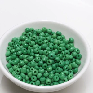 Close-up of 4mm green seed beads in a white bowl for DIY jewelry making material