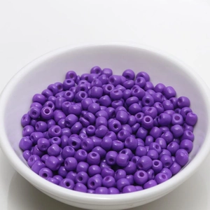 Macro shot of 4mm purple round glass seed beads in a white bowl for DIY jewelry making