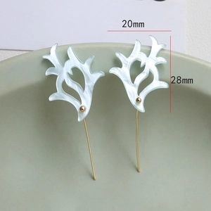 Macro detail of 28mm white acetate antler studs with golden pins on a ceramic dish