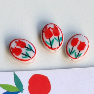Detailed view of oval ceramic beads with hand-painted red tulips for DIY jewelry making