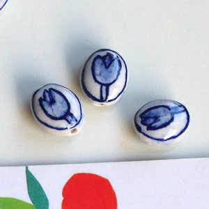 Detail of three handmade ceramic oval beads with hand-painted blue tulips for DIY jewelry