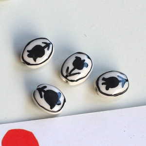 Detailed view of handmade ceramic tulip beads with black floral patterns for DIY jewelry