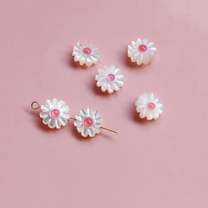 Détail de perles en coquillage marguerite pour bijoux DIY sur fond rose poudré