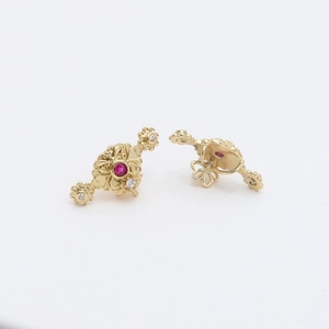 Detail of vintage gold plated earrings with red zircon and floral relief texture