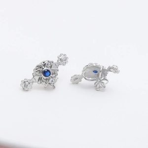 Detail of silver hollowed earrings with dark blue gemstone and floral diamond accents