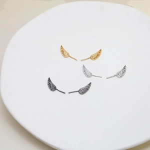 Detailed angel wing stud earrings in gold, silver, and gun black finishes on a white tray