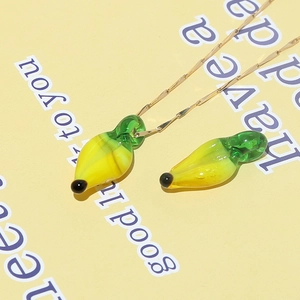 Macro shot of a yellow glass banana pendant with green stem on a gold chain necklace