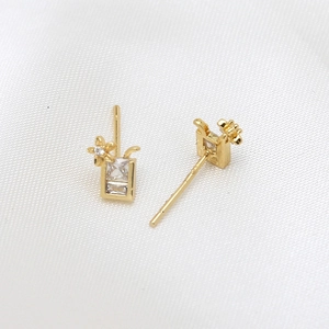 Détail de boucles d'oreilles dorées avec zircon rectangulaire et petite fleur délicate