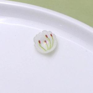Detailed macro view of white floral resin charms with green leaves for DIY jewelry making
