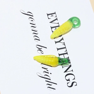 Macro detail of glass corn-shaped charms with yellow kernels and green leaves for DIY jewelry