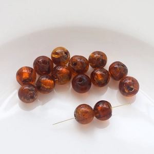 Macro shot of amber glass beads with gold swirls in a white ceramic dish for DIY jewelry