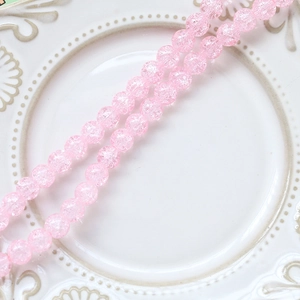 Close-up of pink crackle glass round beads on a white ceramic plate for DIY jewelry