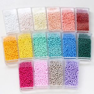 Flat lay of 16-color macaron glass seed beads in organized clear containers for DIY jewelry