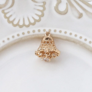 Macro detail of gold-plated hollow filigree bell pendant with dangling clear zircon