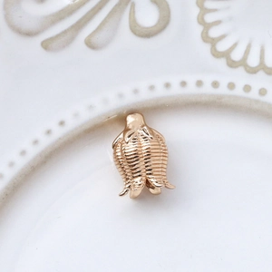 Detailed macro view of a rose gold flower bud pendant with textured stripes on white ceramic