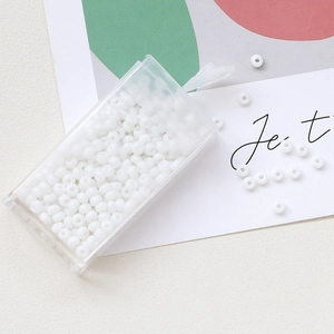 Macro shot of 3mm white macaron glass seed beads in a transparent storage box