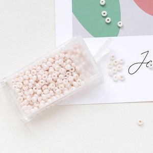 Macro shot of 3mm white macaron glass seed beads in a transparent plastic storage box