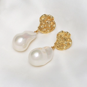 Detail of gold moon-shaped earrings with large baroque pearls on white silk texture