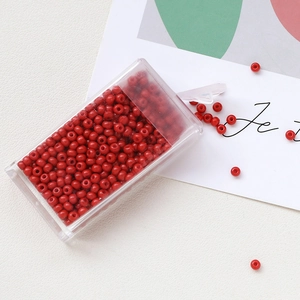 Detailed view of glossy red glass seed beads in a clear storage box for DIY jewelry making