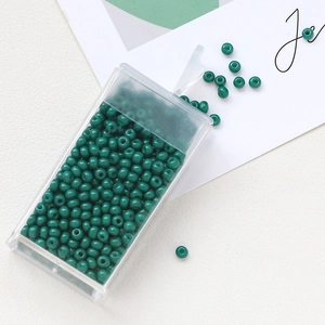 Detail of dark green macaron glass seed beads in a transparent plastic storage box
