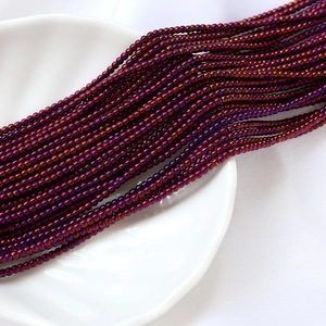 Détail macro de perles de verre violettes 2mm à effet irisé sur un plateau blanc